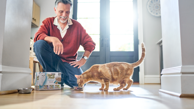 old man watching cat eat in the kitchen