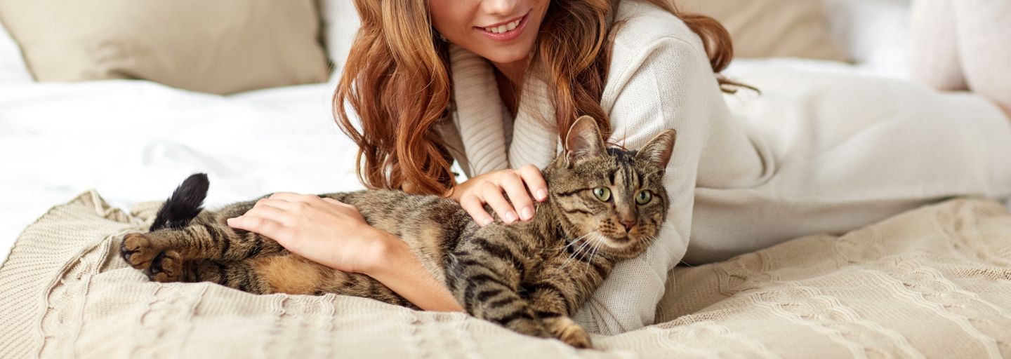 happy young woman with cat lying in bed at home.