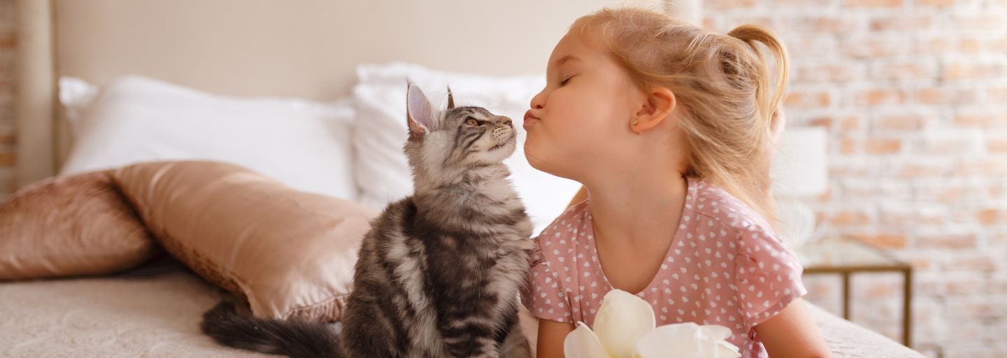 Little girl and cat sitting together on a bed looking at each other 